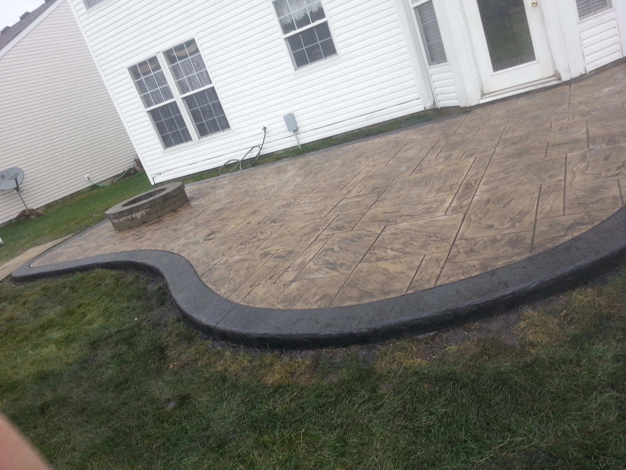 Stamped concrete patio with curved border next to white house