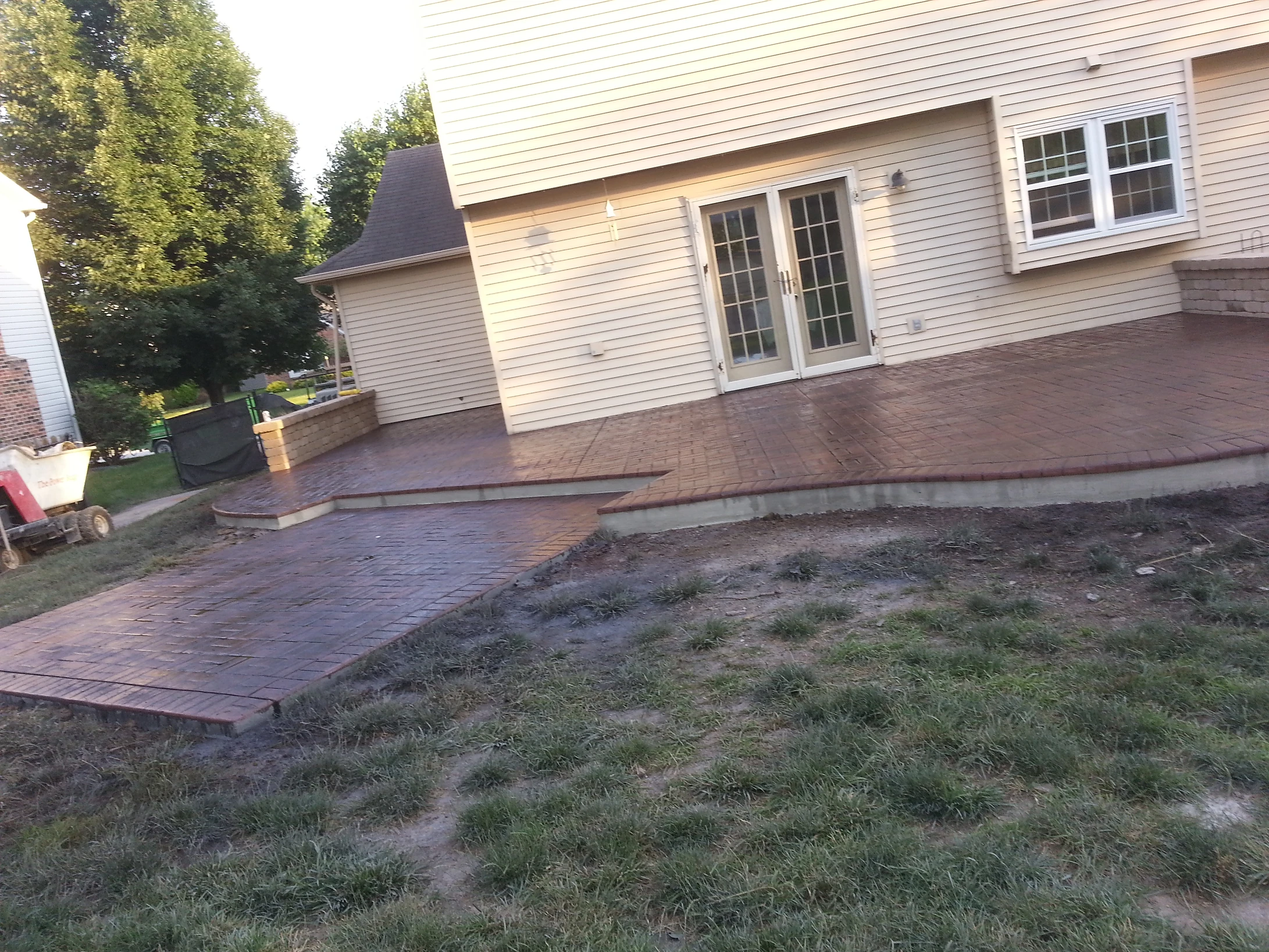 Brick patio with french doors and patchy lawn in suburban backyard