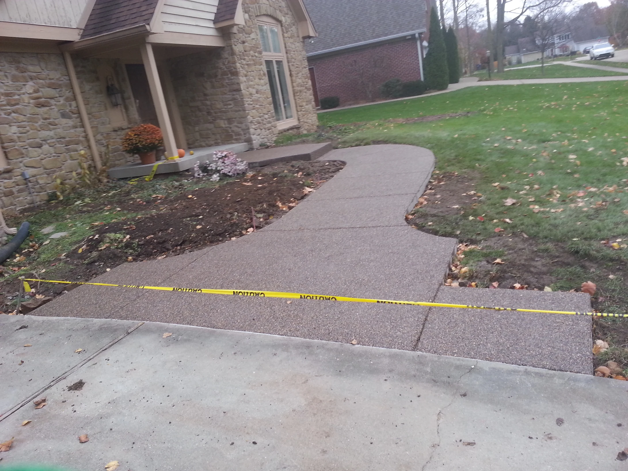Concrete walkway near stone house with caution tape and fallen leaves