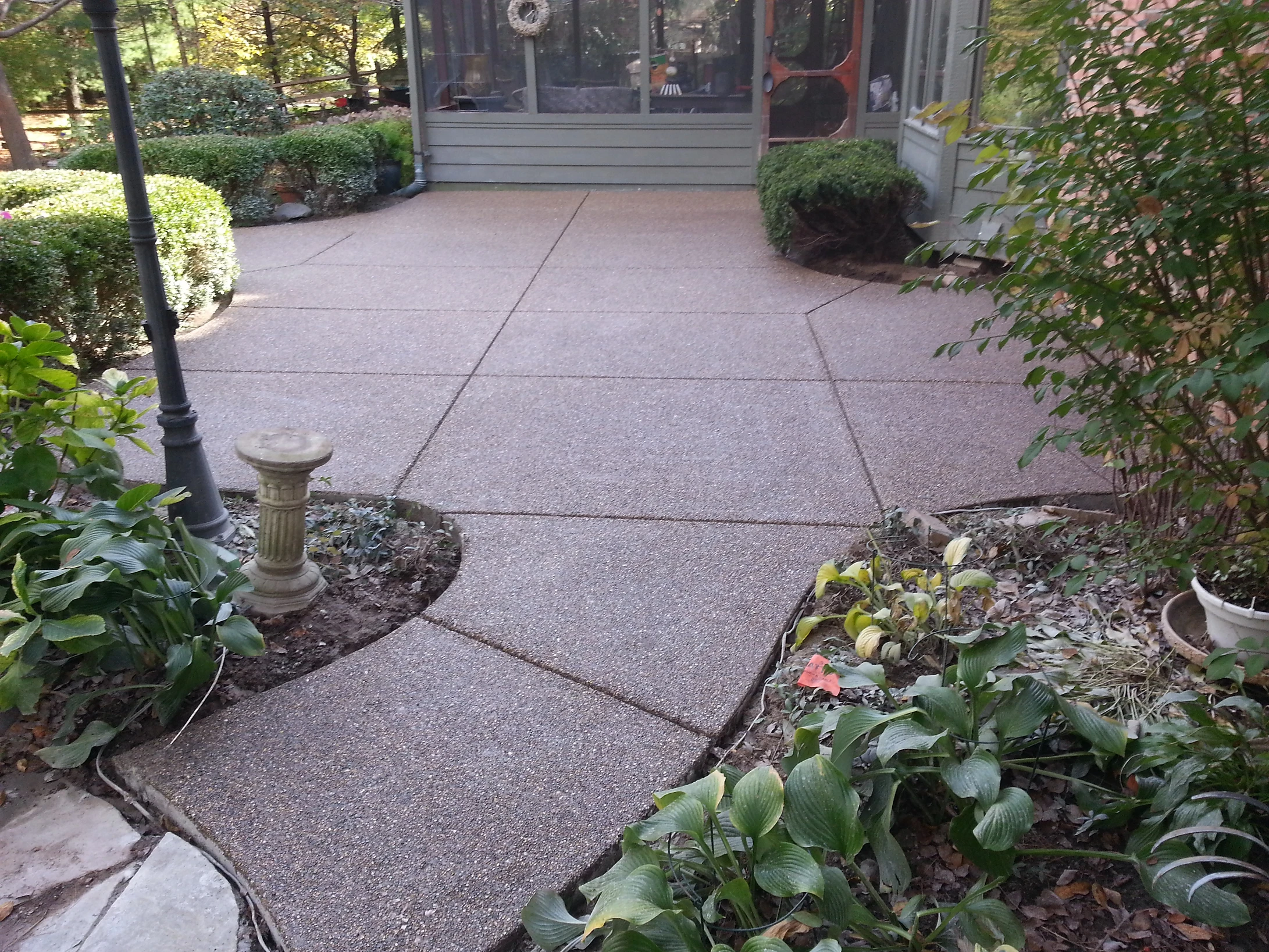 Landscaped patio with concrete walkway, plants, and garden ornament