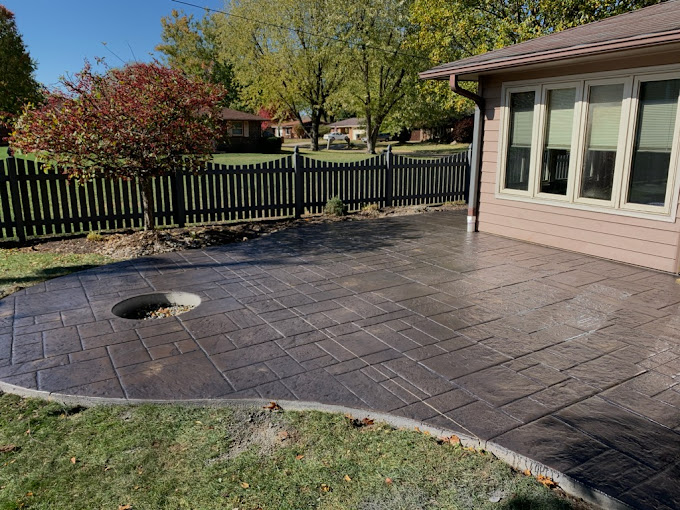 Stamped concrete patio with black fence and trees in suburban backyard