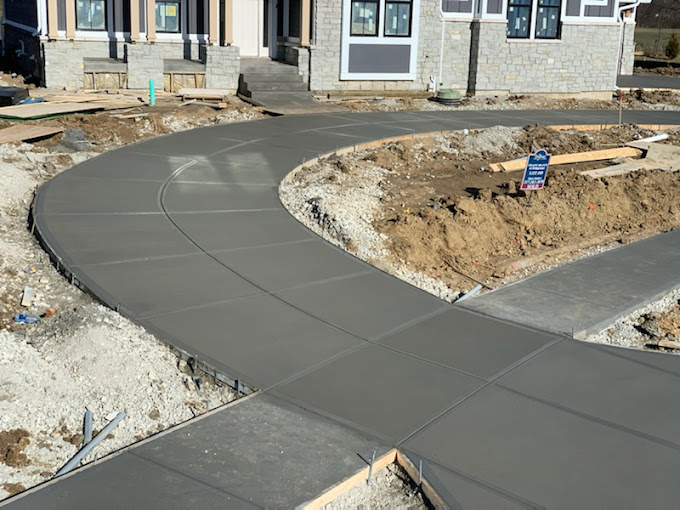 Newly poured curved concrete walkway in front of a stone-faced house construction