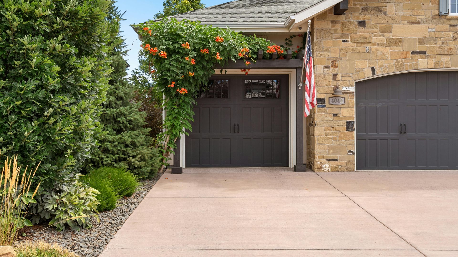 Stone house with dark garage doors, flowering vines, and American flag